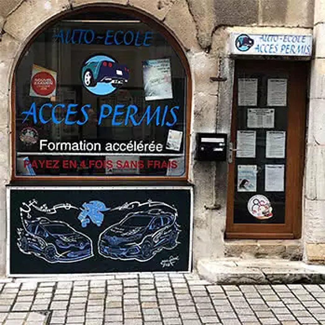 Devanture en pierre de l’agence Pasteur : vitrine arrondie au lettrage bleu « Accès Permis » et porte vitrée couverte d’affichettes.